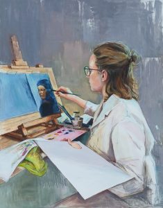 Pintura «El proceso»: una joven con gafas y camisa blanca pinta un retrato en un caballete, con paleta, pinceles y papeles en la mesa, ante un fondo gris
