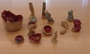 Conjunto cerámico «Abrir un espacio»: piezas pequeñas de barro arenoso, cuencos y formas verticales, algunas esmaltadas en rojo, sobre una mesa de madera