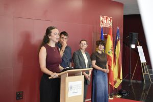 A speaker at the lectern during the 20th Artistic Creation Competition prize-giving in the Student Recreation Centre hall, with flags in the background