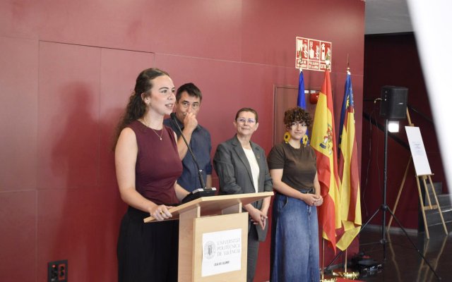 A speaker at the lectern during the 20th Artistic Creation Competition prize-giving in the Student Recreation Centre hall, with flags in the background