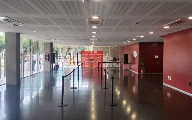Vestíbul de la Casa de l'Estudiant preparat per a la jornada d'acollida, amb faristol, banderes i photocall roig d'UPV PIAE+ al fons