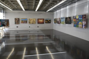 Sala de exposición con pinturas colgadas en las paredes, varias con patatas como motivo, del reto creativo de Patatas Lázaro para Bellas Artes