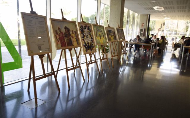Cavallets de fusta amb les obres de l'exposició Konngol Rewbe de l'ONG AIDA i un panell informatiu al vestíbul de la Casa de l'Estudiant