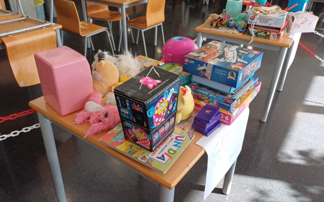 Taula amb joguets donats en la campanya Un Juguete, una Sonrisa: una caixa de Lego, peluixos, trencaclosques, jocs de taula i un llibre infantil