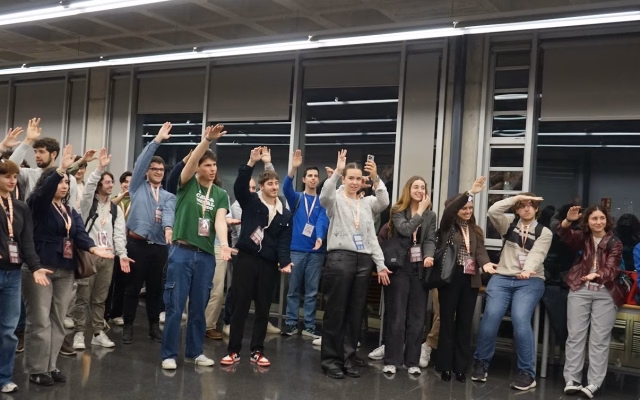 Participants at the 7th CREUP-CRUE Congress, wearing lanyards, raise their hands during an activity at the Student Recreation Centre