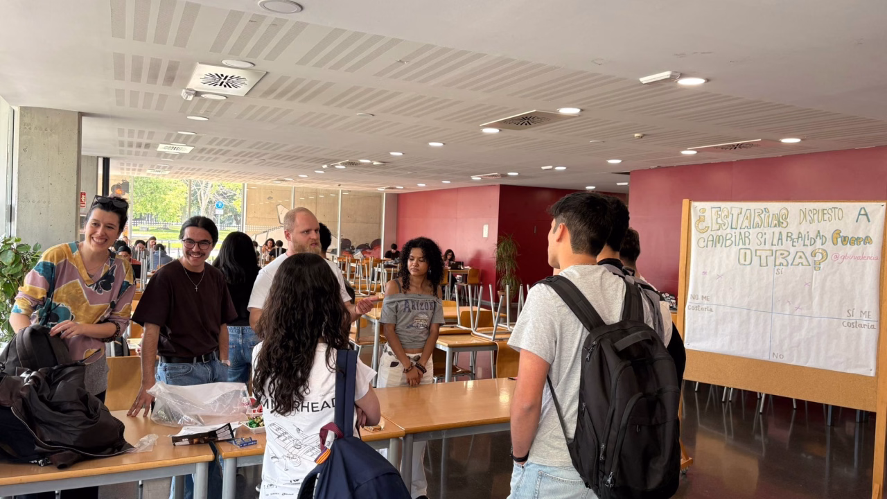 Estudiants conversen a la taula informativa del Grupo Bíblico Universitario, a la planta baixa de la Casa de l'Estudiant, al costat d'un panell d'enquesta