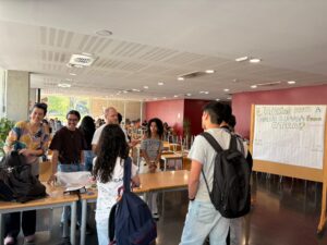 Estudiants conversen a la taula informativa del Grupo Bíblico Universitario, a la planta baixa de la Casa de l'Estudiant, al costat d'un panell d'enquesta