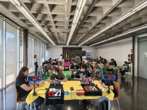 Participantes resuelven cubos de Rubik con cronómetros de speedcubing en mesas con manteles amarillos y verdes durante el UPV Open 2026