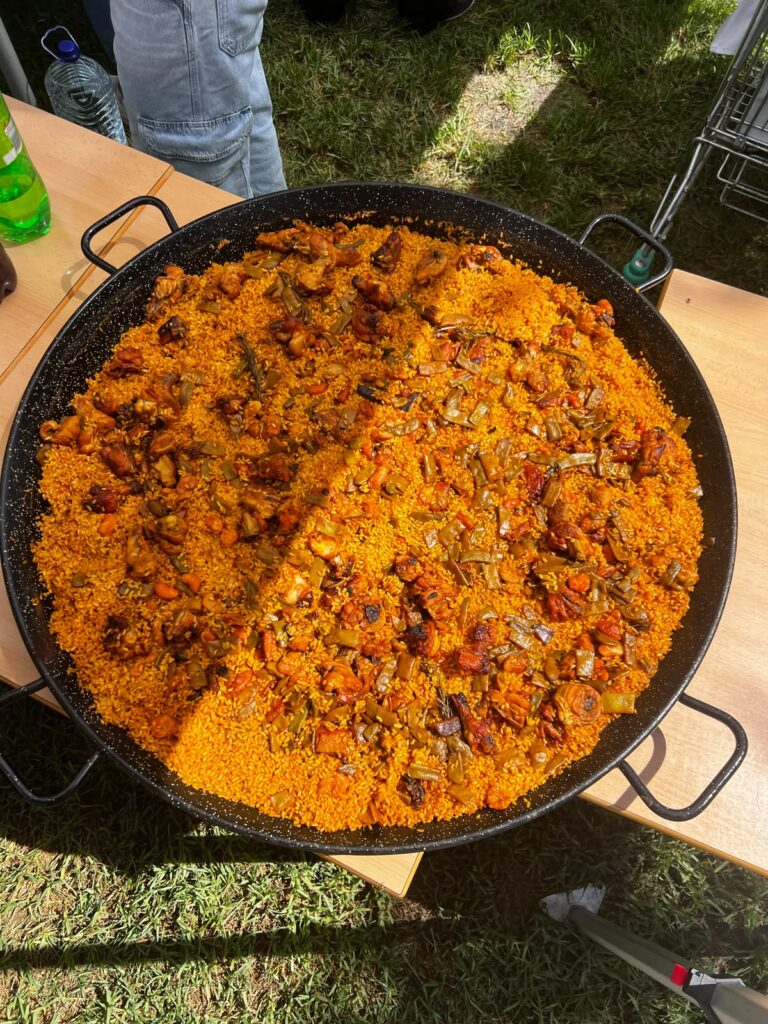 Una gran paella con carne y judías verdes sobre una mesa en el césped durante el Welcome Day