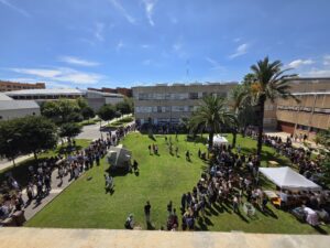 Elevated view of a lawn with large numbers of students in long queues during Welcome Day, with white tents and palm trees