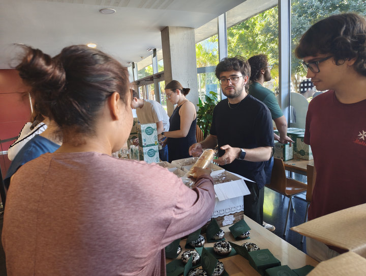 Un estudiant dona un fartó a una estudiant a la taula de l'orxatada, amb dònuts sobre tovallons verds