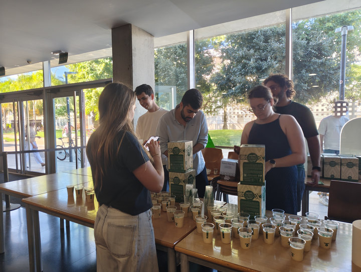 Estudiants preparen desenes de gots d'orxata en taules al costat de la façana de vidre de la planta baixa, amb caixes d'orxata