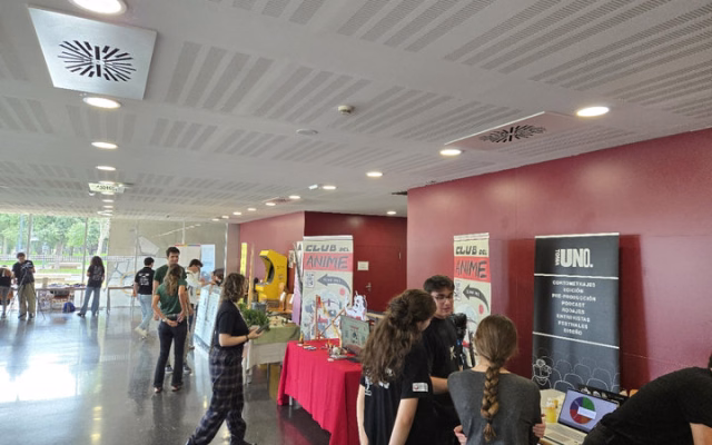 Estudiantes en los estands de la feria en la planta baja de la Casa del Estudiante, con carteles del Club del Anime y de un grupo audiovisual