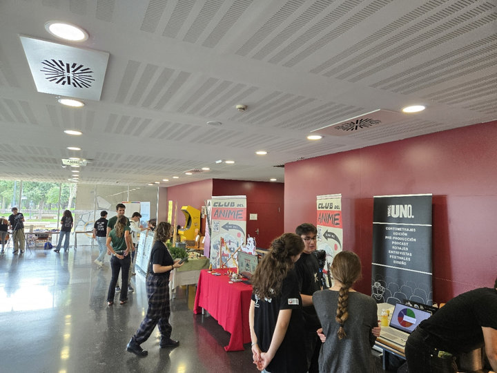 Estudiantes en los estands de la feria en la planta baja de la Casa del Estudiante, con carteles del Club del Anime y de un grupo audiovisual
