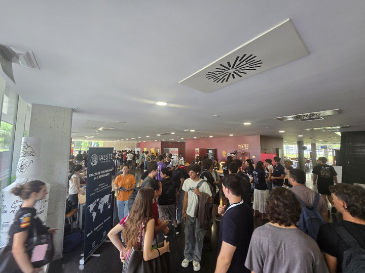 La planta baja de la Casa del Estudiante llena de estudiantes durante la feria, con un cartel enrollable de IAESTE en primer plano