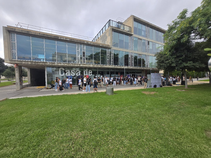Exterior de la Casa del Estudiante con numerosos estudiantes ante la fachada durante la feria y césped en primer plano