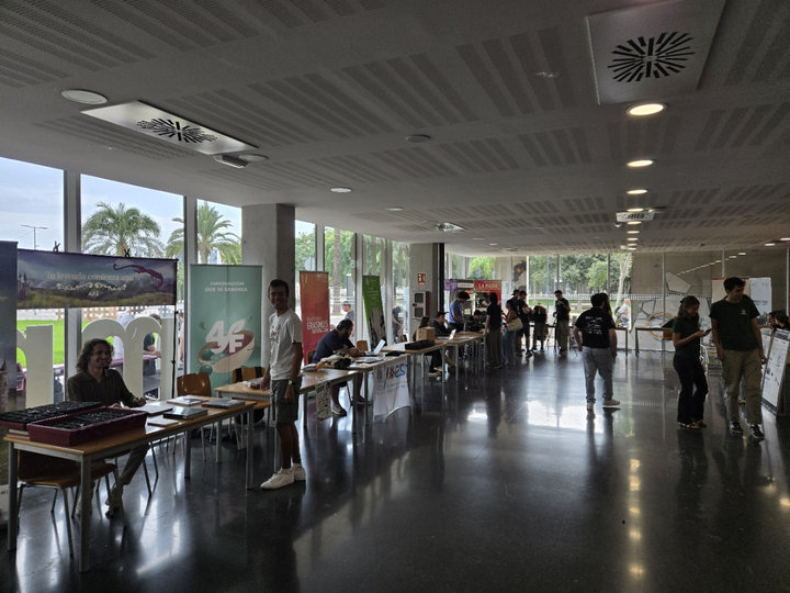 Fila de estands de la feria con mesas y carteles enrollables junto a los ventanales de la planta baja de la Casa del Estudiante